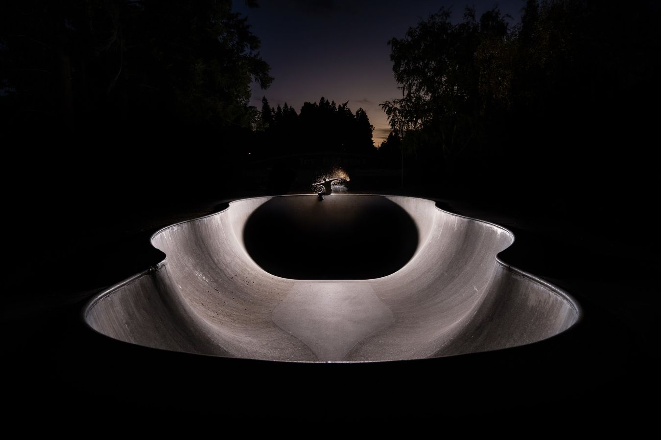 Skater lit on the far lip of a concrete bowl at night