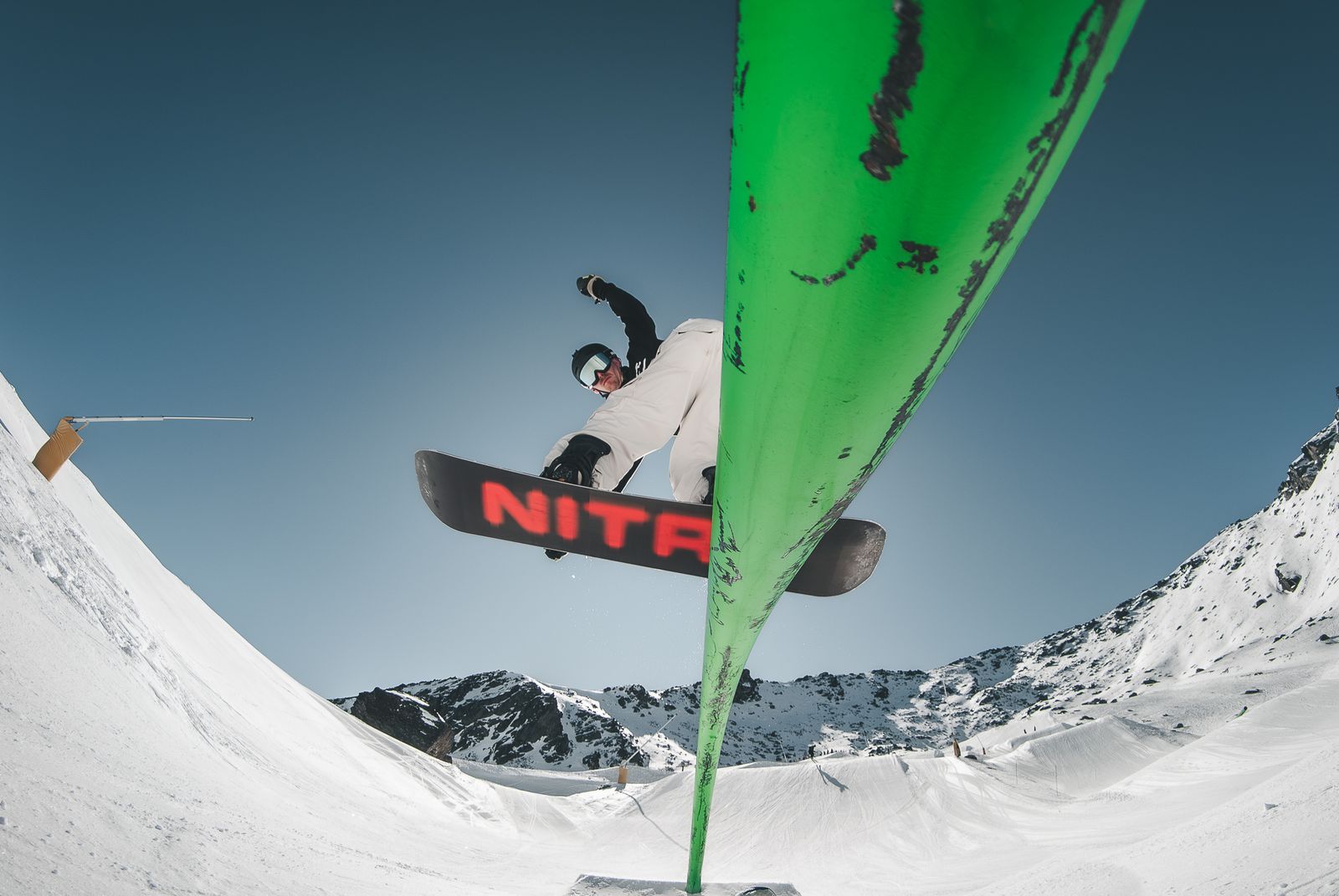 Snowboarder over a green rail against a blue sky