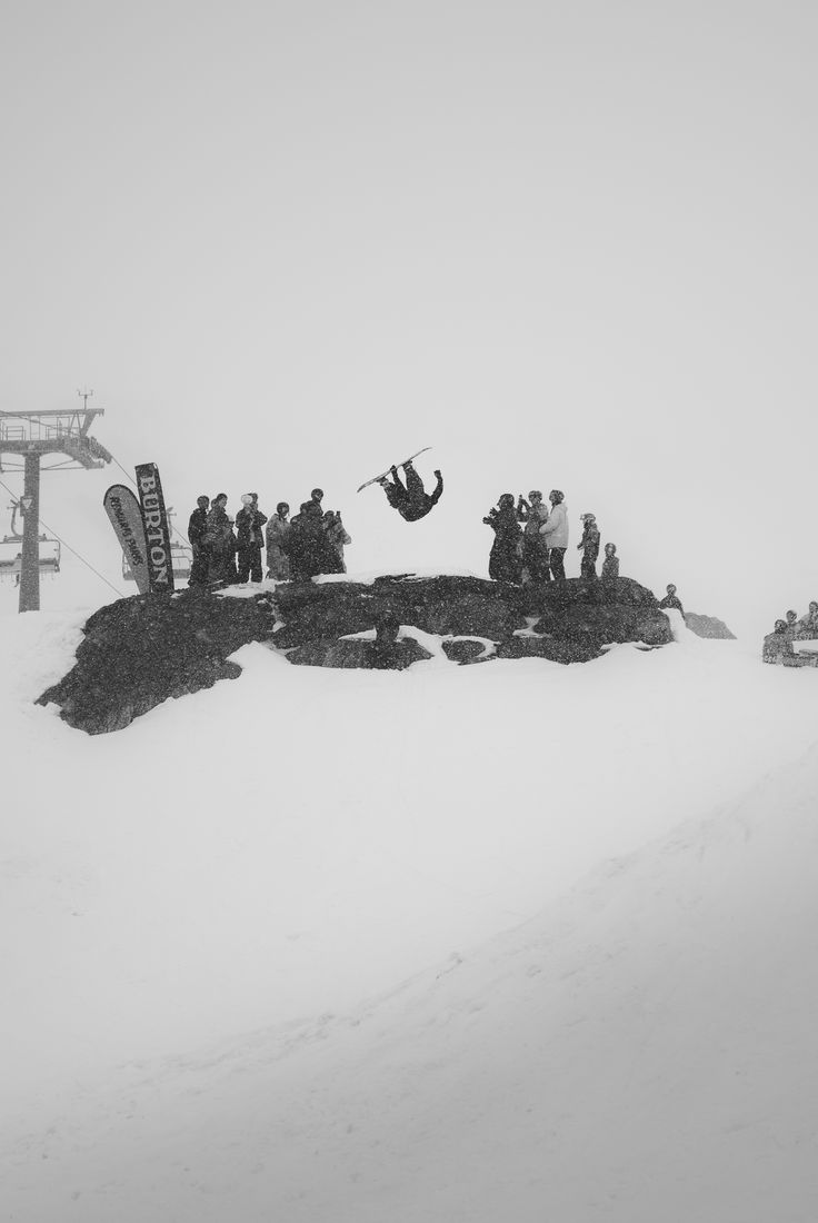 Black and white snowboard backflip over a rock with a crowd watching