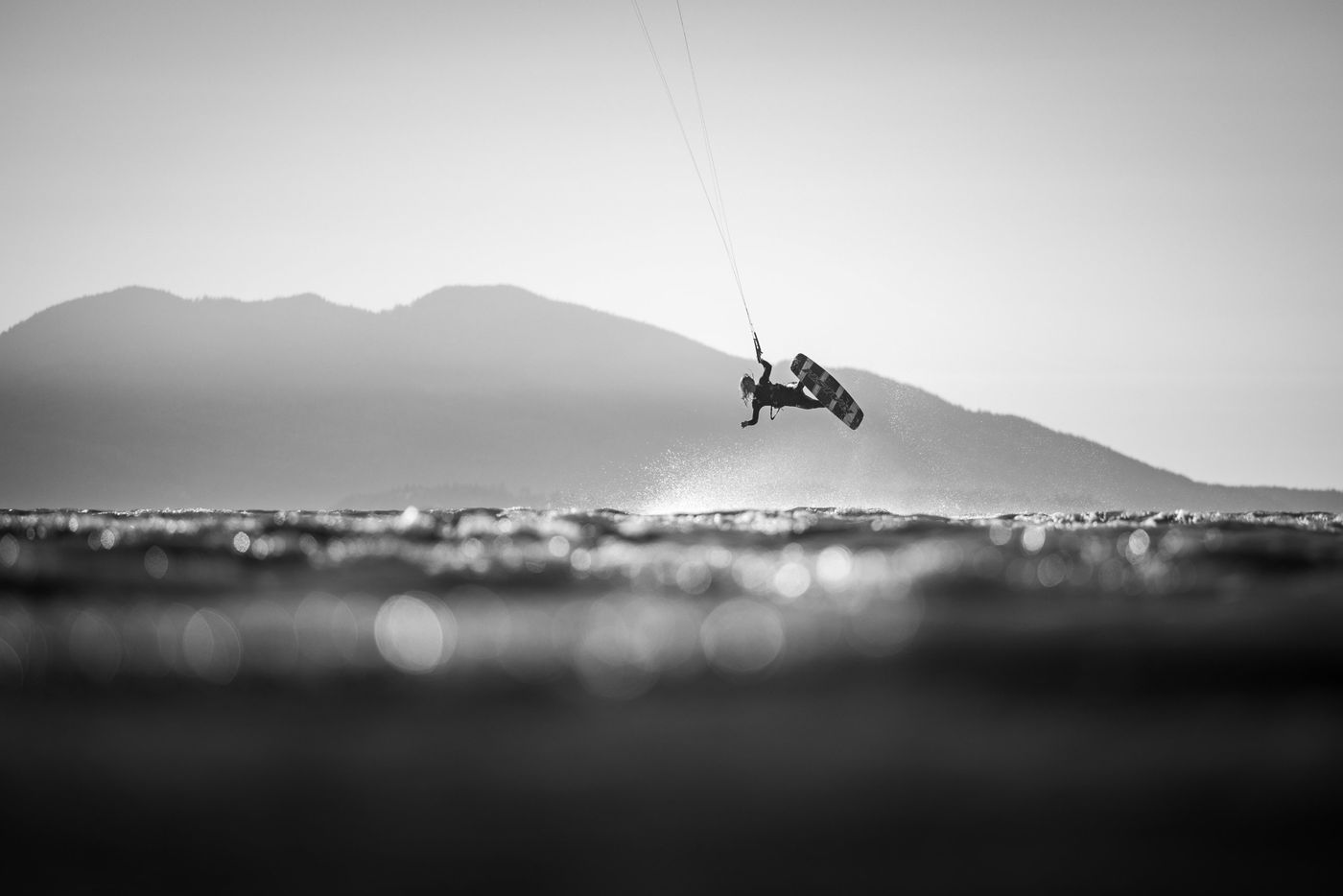 Black and white kitesurfer mid air above the water