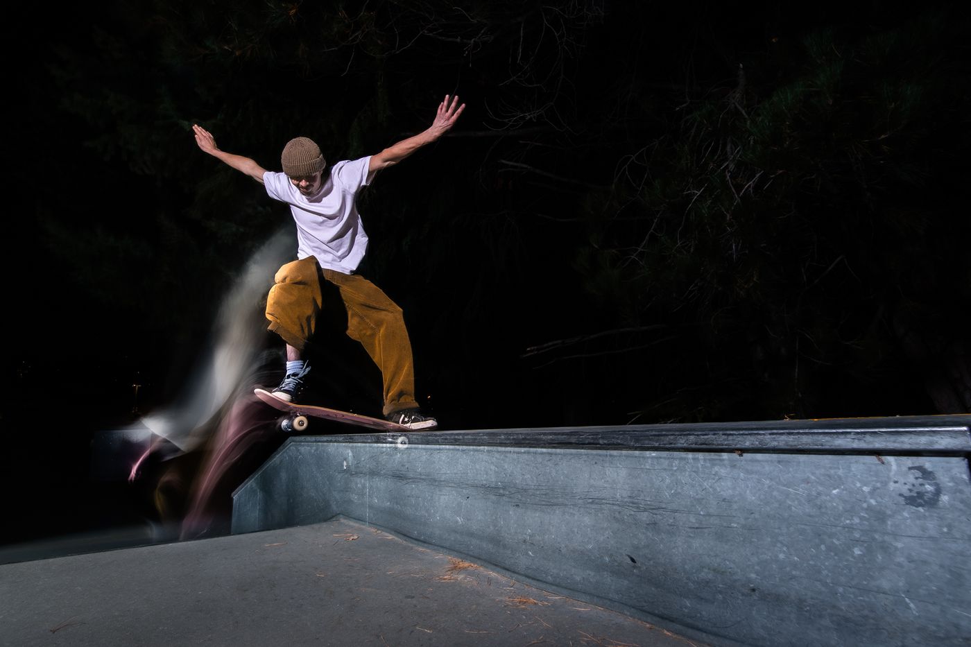 Skater on a ledge at night lit by flash with motion trails