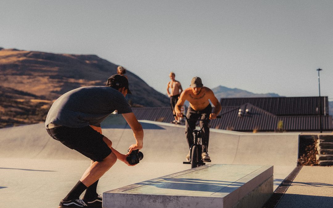 Blake crouched low with a camera as a BMX rider rolls toward a ledge